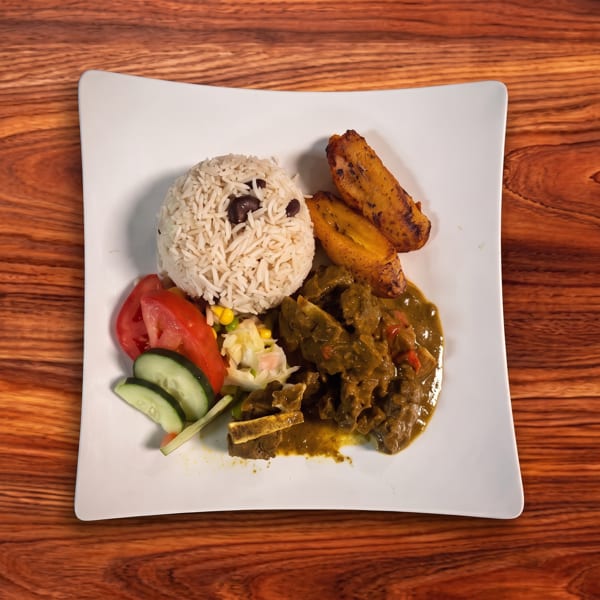Curried goat with rice and peas, fried plantains, and a side salad on a white plate.