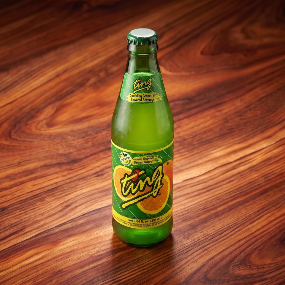 A green bottle of Ting Sparkling Grapefruit Flavored Beverage stands on a rich wooden surface.