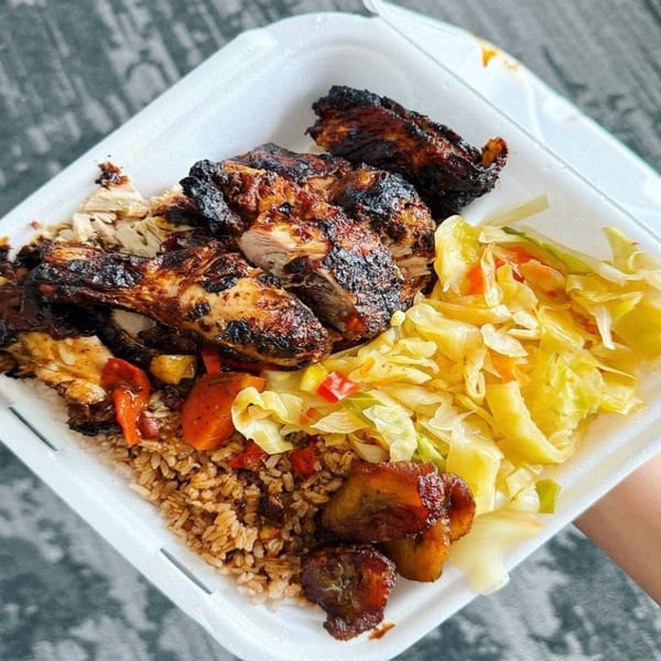 A takeout container filled with jerk chicken, rice and peas, steamed cabbage, and plantains.