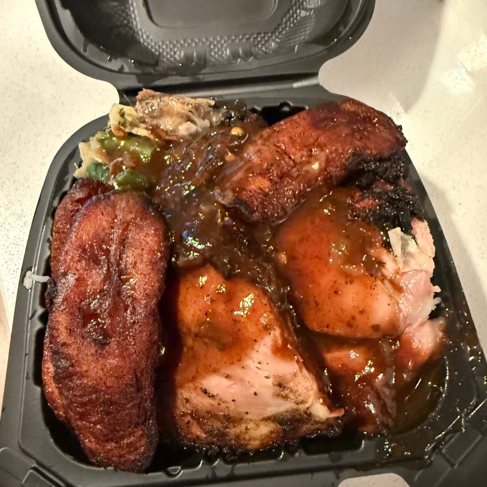 Takeout container with jerk chicken, plantains, and cabbage, covered in a rich brown sauce.