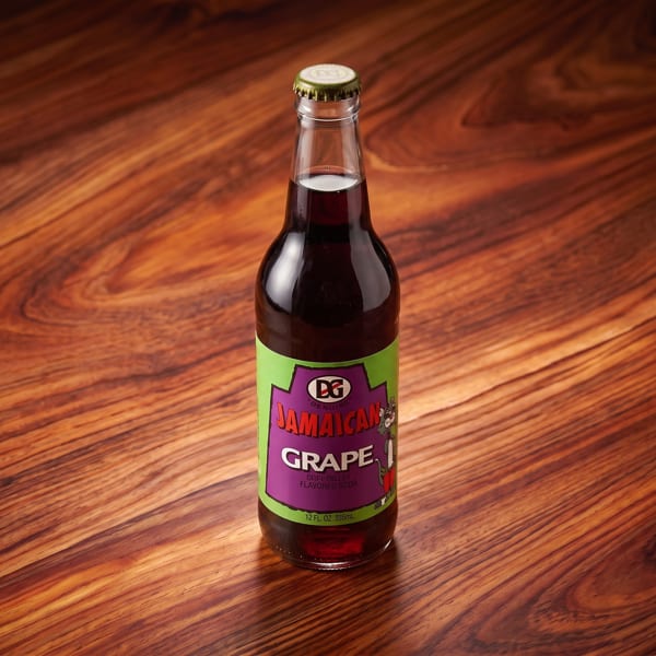 Bottled Jamaican grape-flavored soda with a colorful green and purple label on a wooden table.