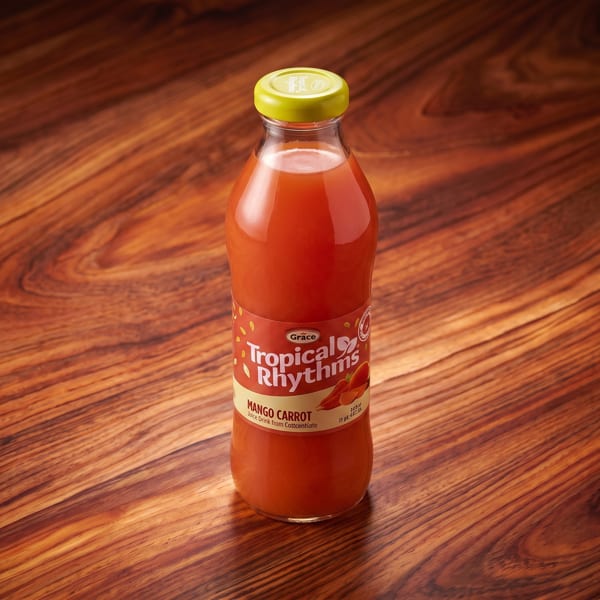 Grace Tropical Rhythms Mango Carrot juice bottle with a yellow cap on a wooden surface.